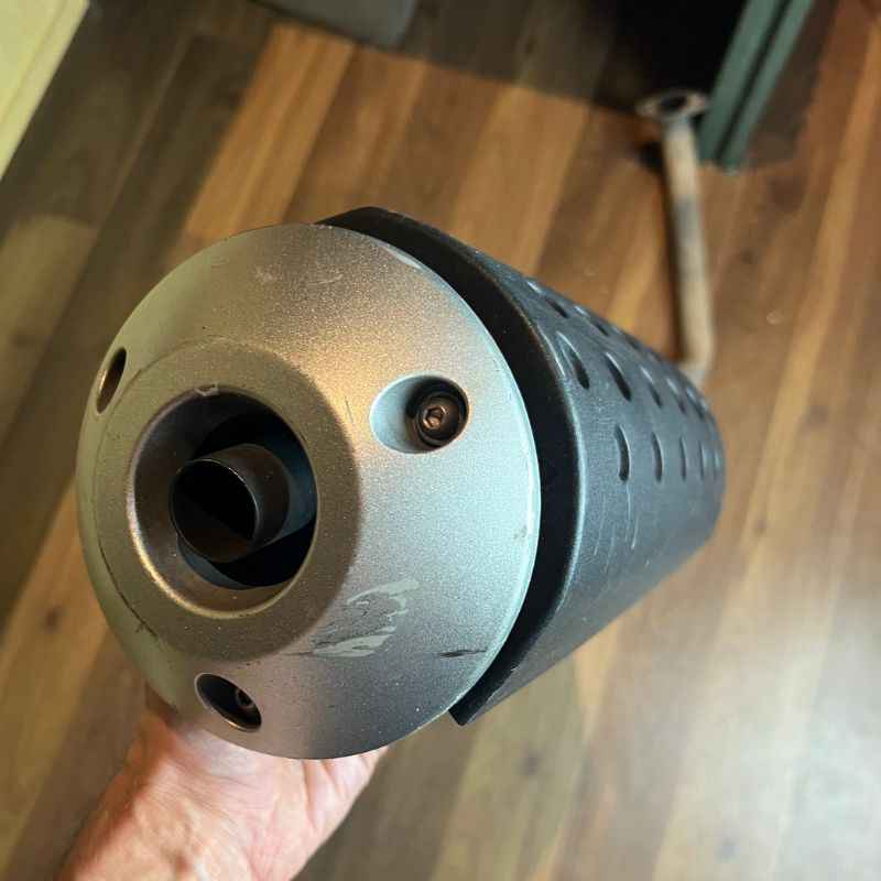 Close-up of the original Yamaha XSR155 OEM exhaust outlet and end cap. Genuine factory muffler removed from the Neo Muscle project motorcycle, showing the original exhaust tip and finish.