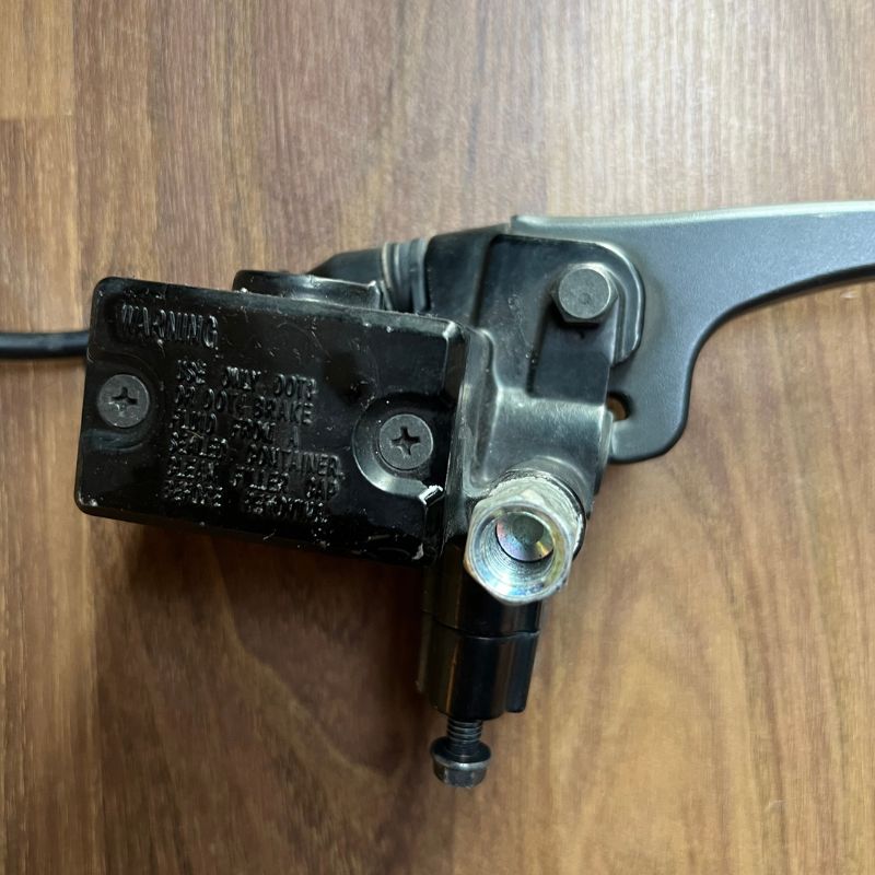 Close-up of the original Yamaha XSR155 OEM front brake master cylinder and brake lever assembly removed from the Neo Muscle project motorcycle. Genuine factory front brake lever, master cylinder and reservoir for OEM replacement or stock restoration.