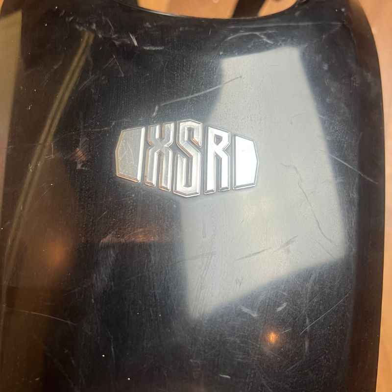 Close-up of the original Yamaha XSR155 OEM upper tank cover showing the factory XSR logo and surface condition. Genuine Yamaha fuel tank cover removed from the Neo Muscle project motorcycle with light cosmetic scratches from normal use.